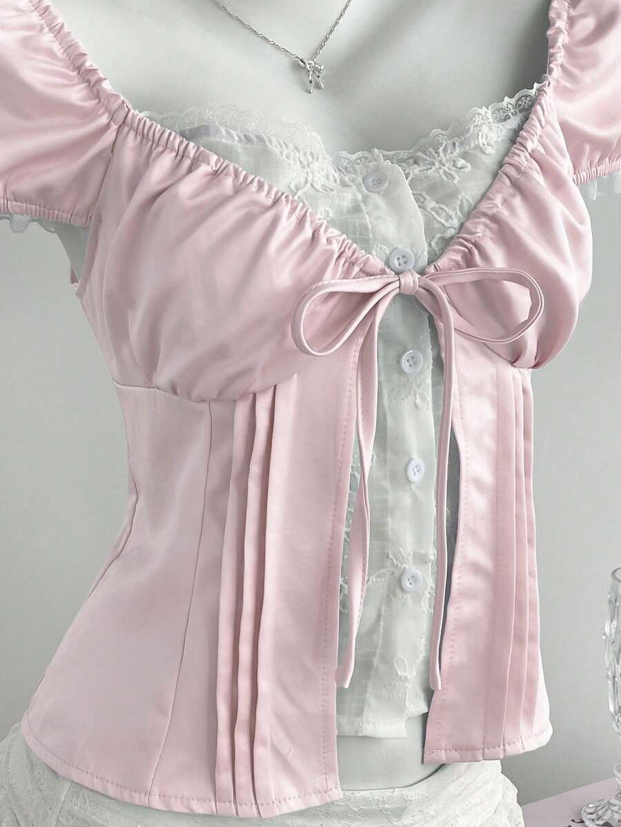 Women's black 2-in-1 blouse featuring a sweetheart neckline, short puff sleeves, front tie bow accent, and asymmetrical hem.