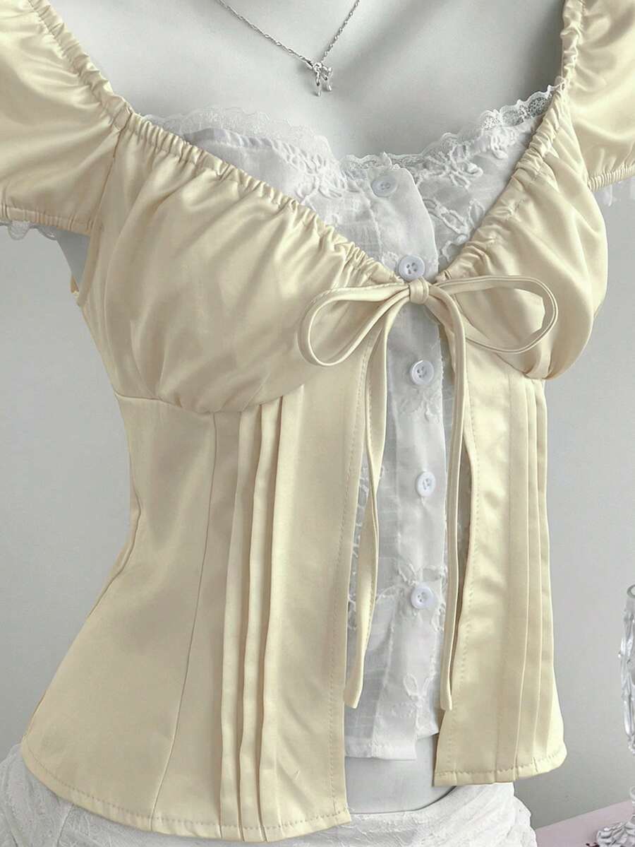 Women's black 2-in-1 blouse featuring a sweetheart neckline, short puff sleeves, front tie bow accent, and asymmetrical hem.