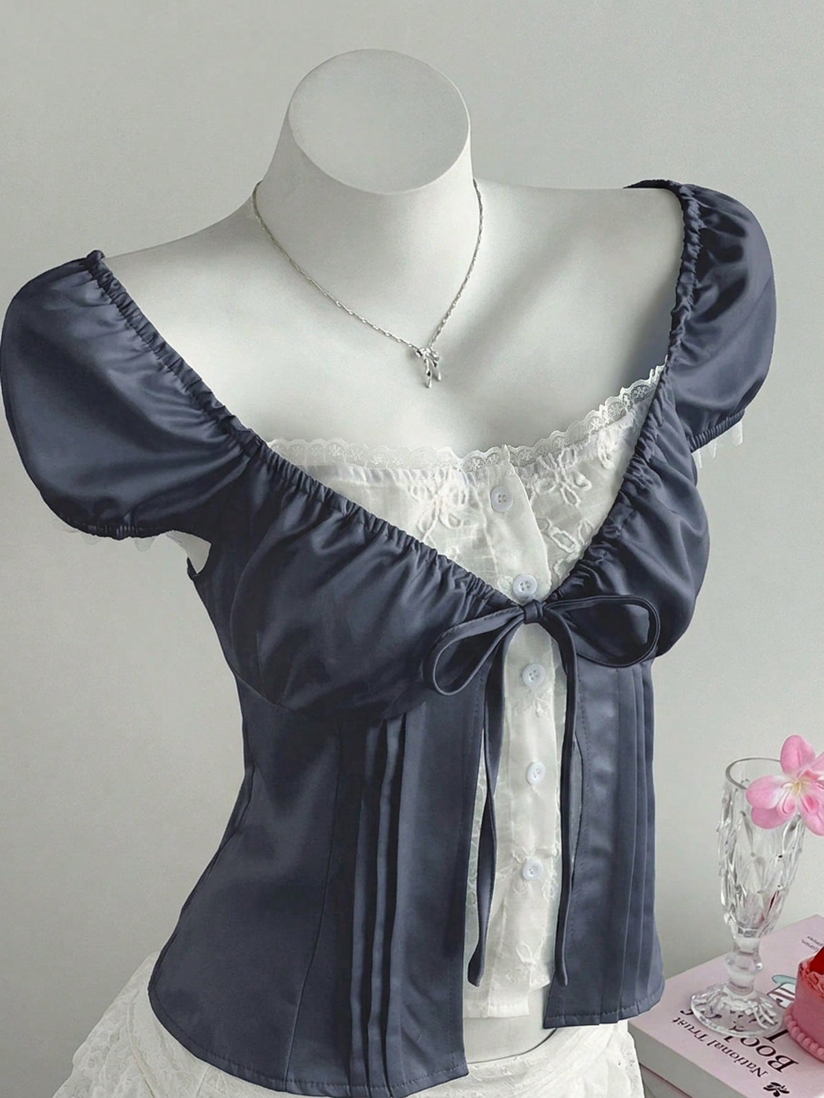 Women's black 2-in-1 blouse featuring a sweetheart neckline, short puff sleeves, front tie bow accent, and asymmetrical hem.