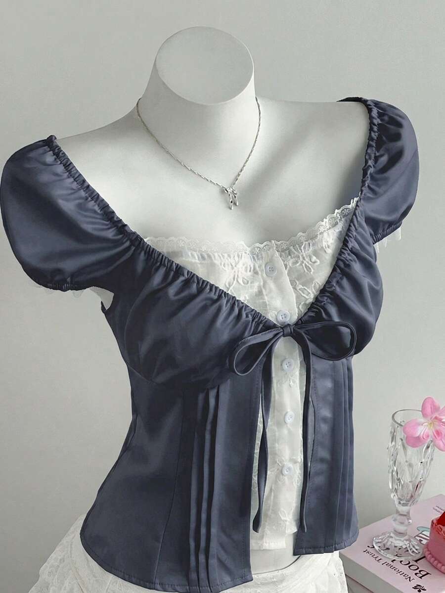 Women's black 2-in-1 blouse featuring a sweetheart neckline, short puff sleeves, front tie bow accent, and asymmetrical hem.