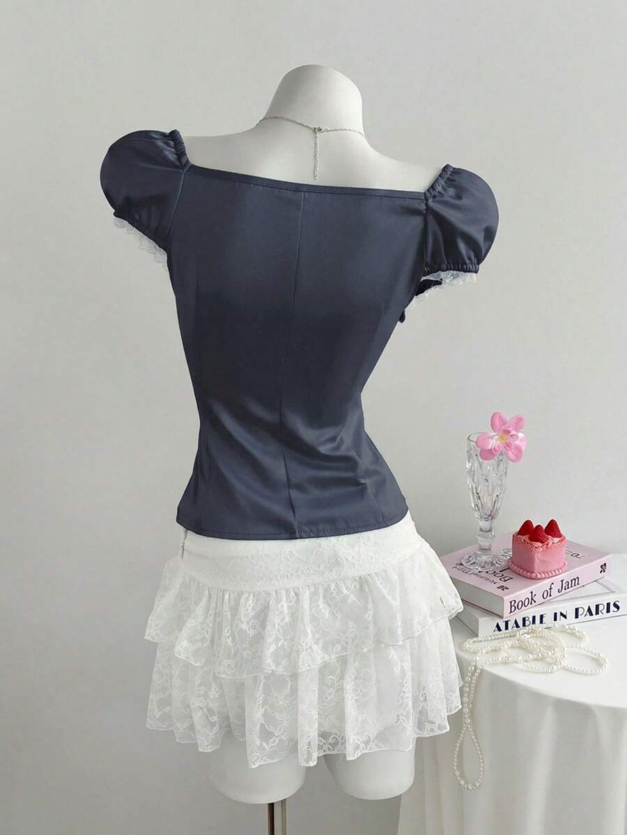 Women's black 2-in-1 blouse featuring a sweetheart neckline, short puff sleeves, front tie bow accent, and asymmetrical hem.