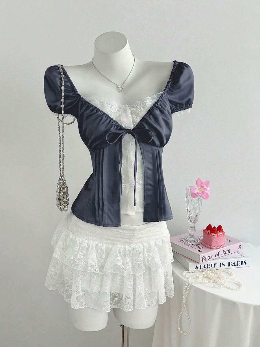 Women's black 2-in-1 blouse featuring a sweetheart neckline, short puff sleeves, front tie bow accent, and asymmetrical hem.