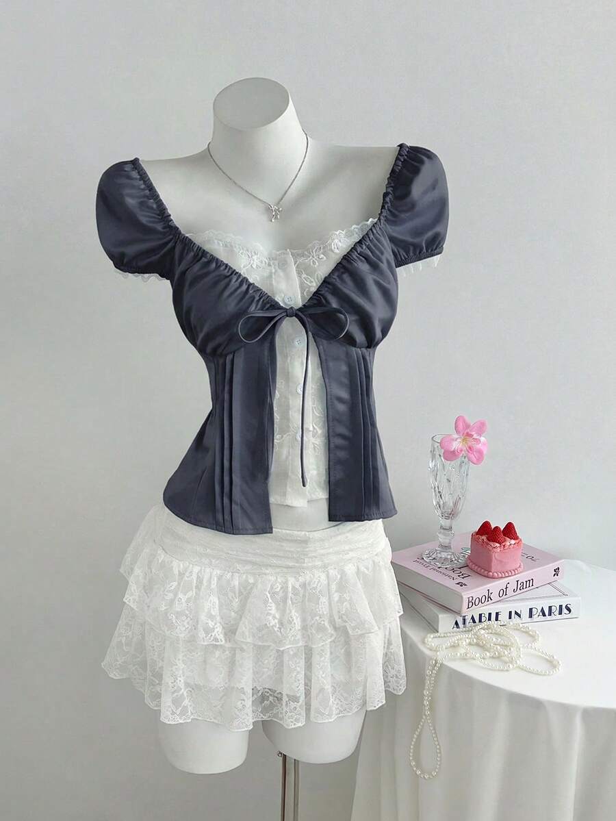 Women's black 2-in-1 blouse featuring a sweetheart neckline, short puff sleeves, front tie bow accent, and asymmetrical hem.