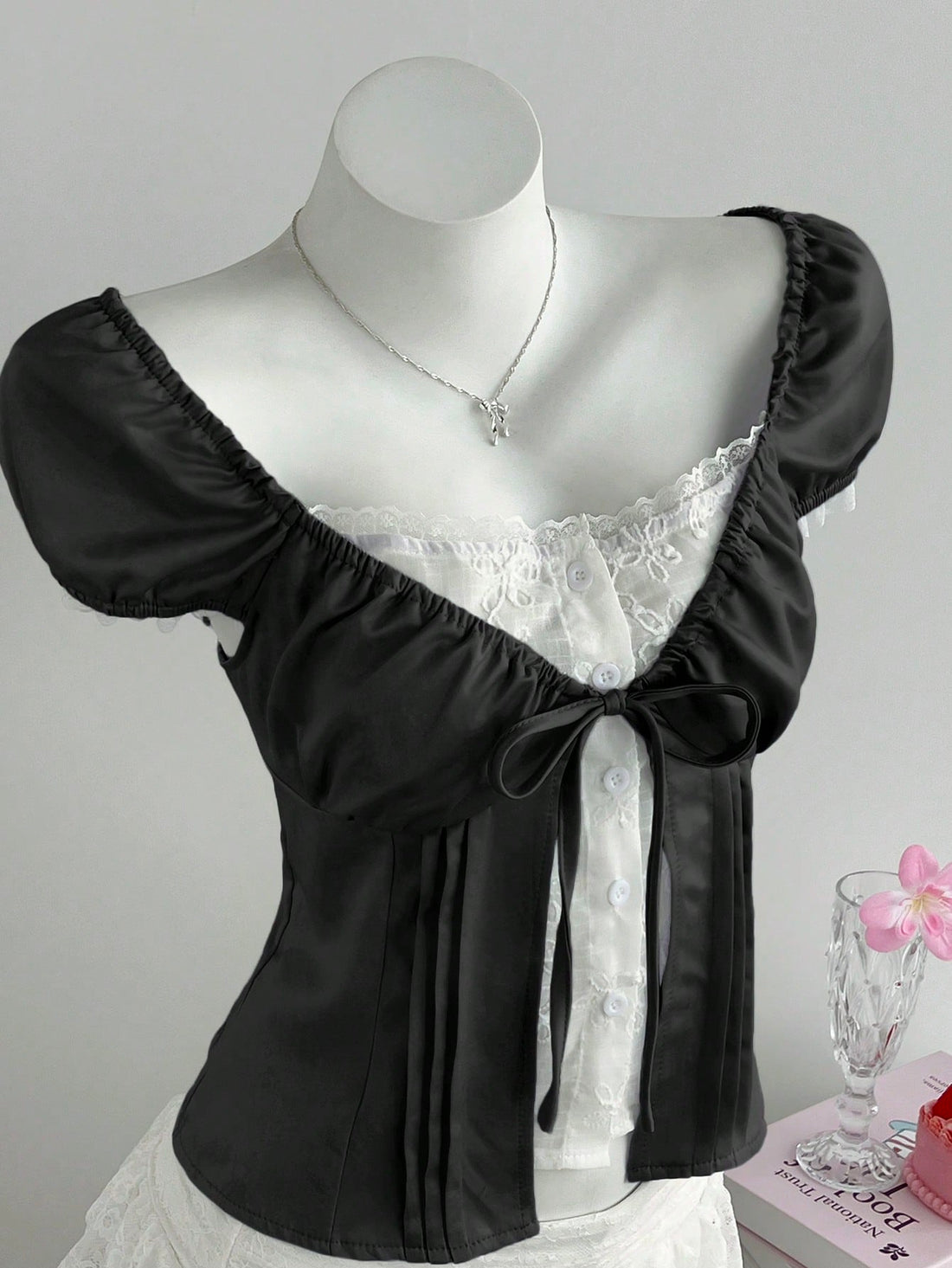Women's black 2-in-1 blouse featuring a sweetheart neckline, short puff sleeves, front tie bow accent, and asymmetrical hem.