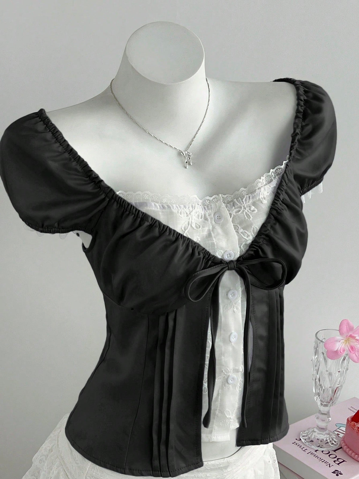 Women's black 2-in-1 blouse featuring a sweetheart neckline, short puff sleeves, front tie bow accent, and asymmetrical hem.