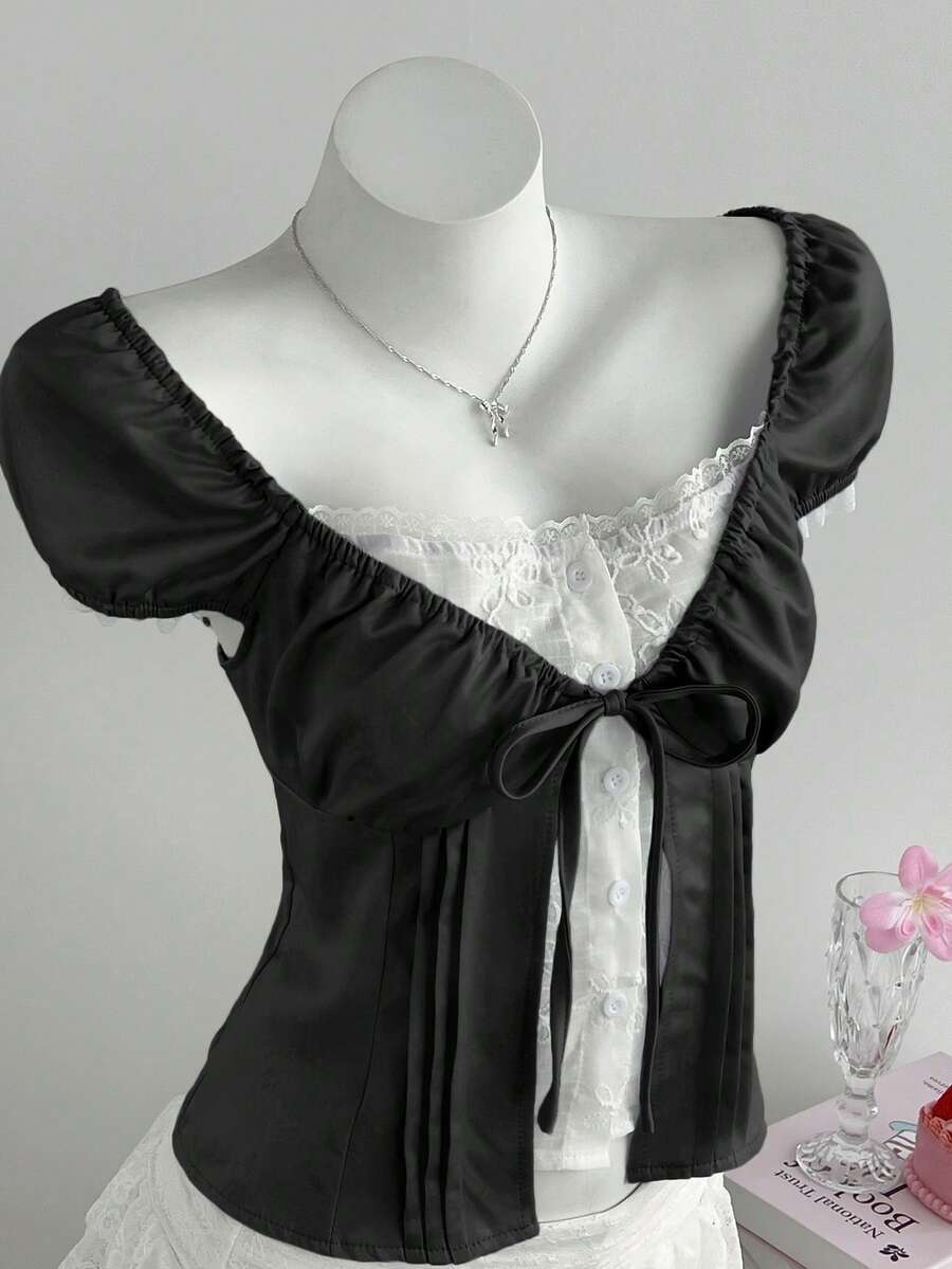 Women's black 2-in-1 blouse featuring a sweetheart neckline, short puff sleeves, front tie bow accent, and asymmetrical hem.