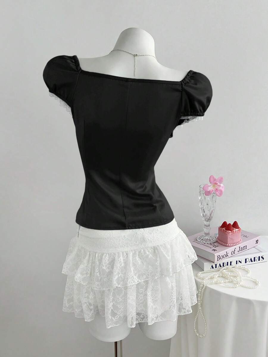 Women's black 2-in-1 blouse featuring a sweetheart neckline, short puff sleeves, front tie bow accent, and asymmetrical hem.