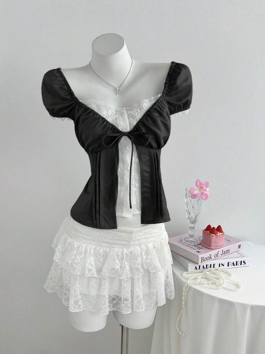 Women's black 2-in-1 blouse featuring a sweetheart neckline, short puff sleeves, front tie bow accent, and asymmetrical hem.