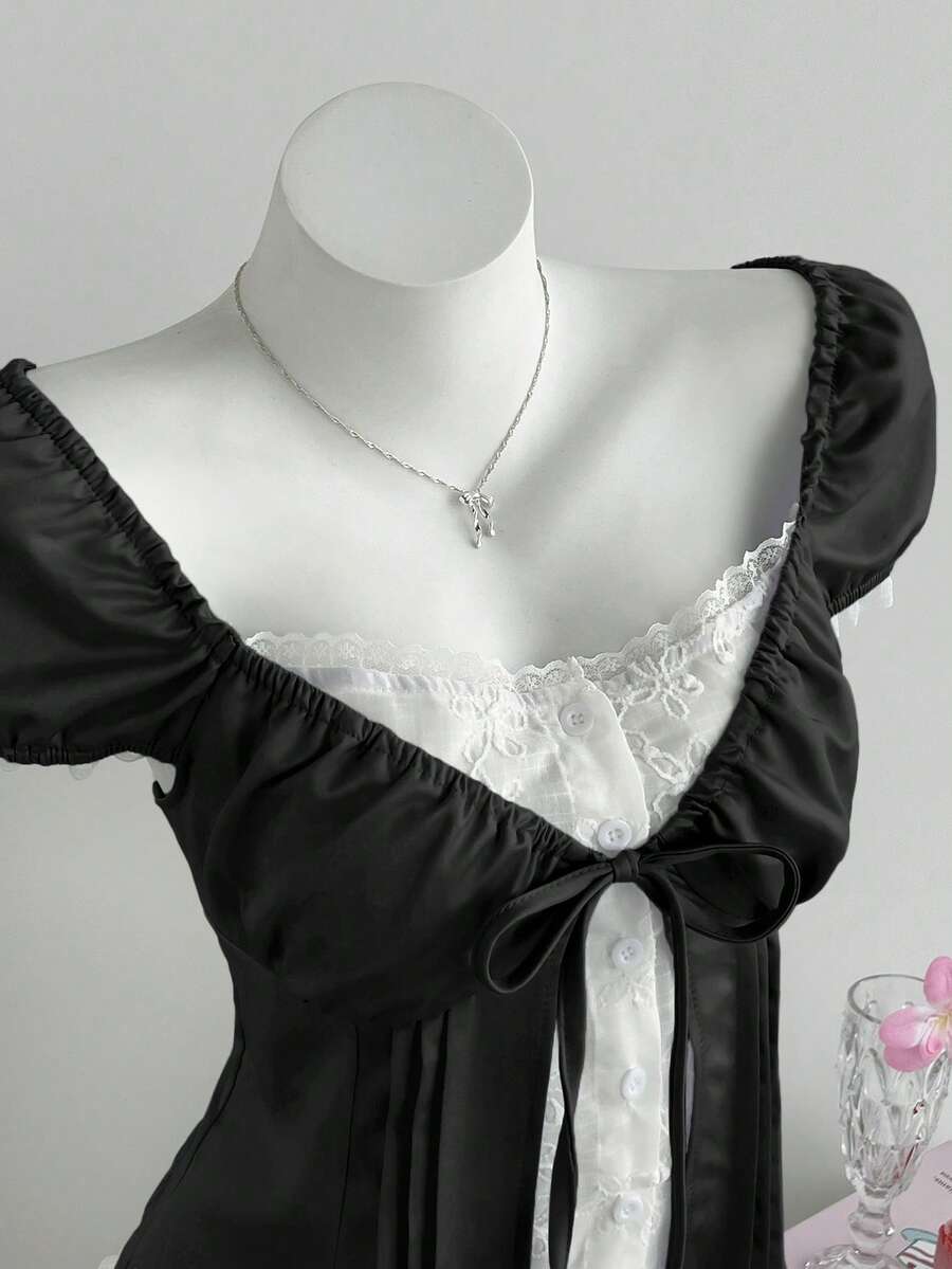 Women's black 2-in-1 blouse featuring a sweetheart neckline, short puff sleeves, front tie bow accent, and asymmetrical hem.