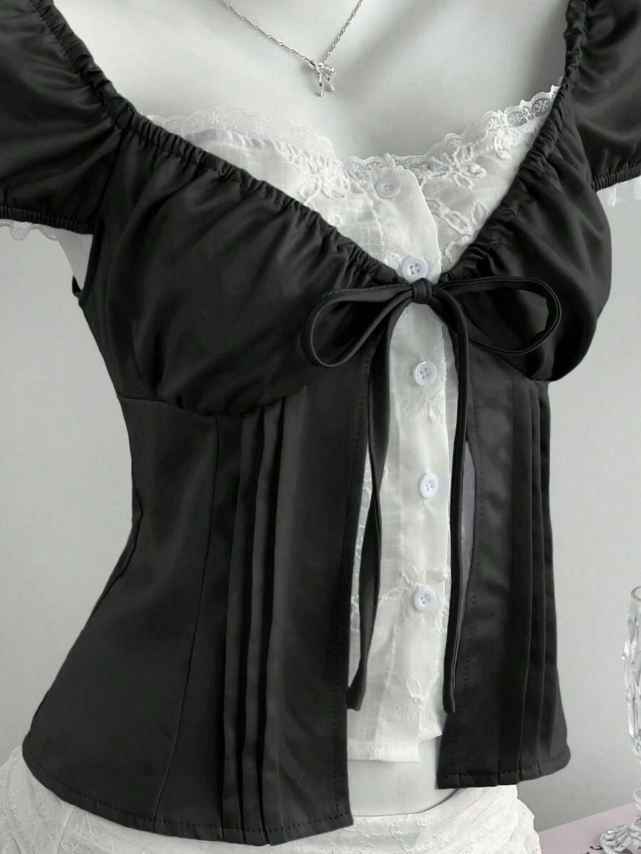 Women's black 2-in-1 blouse featuring a sweetheart neckline, short puff sleeves, front tie bow accent, and asymmetrical hem.