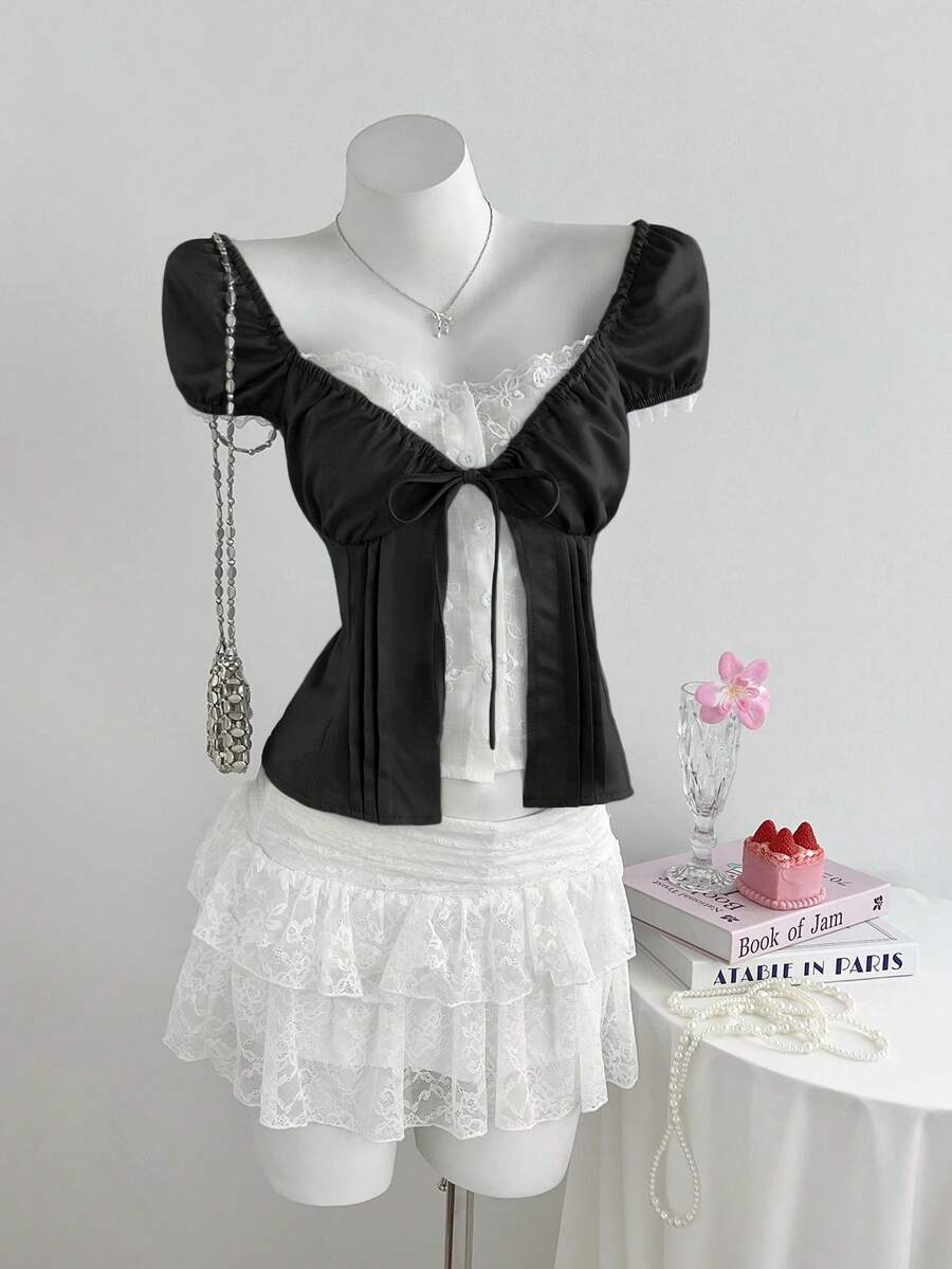 Women's black 2-in-1 blouse featuring a sweetheart neckline, short puff sleeves, front tie bow accent, and asymmetrical hem.