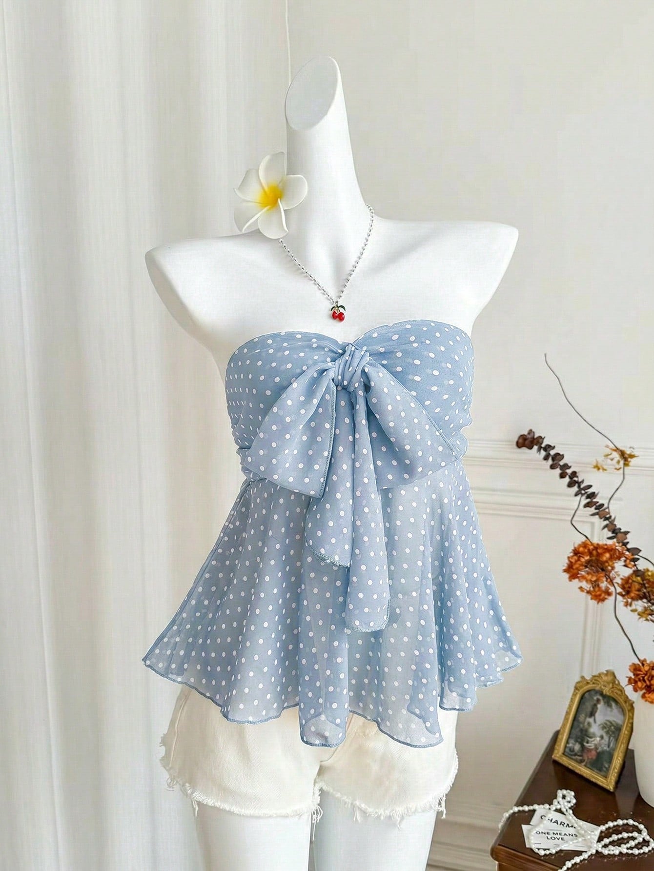 Women's polka dot strapless bandeau crop top with tie bow detail, asymmetrical shirring, and a flared hem.