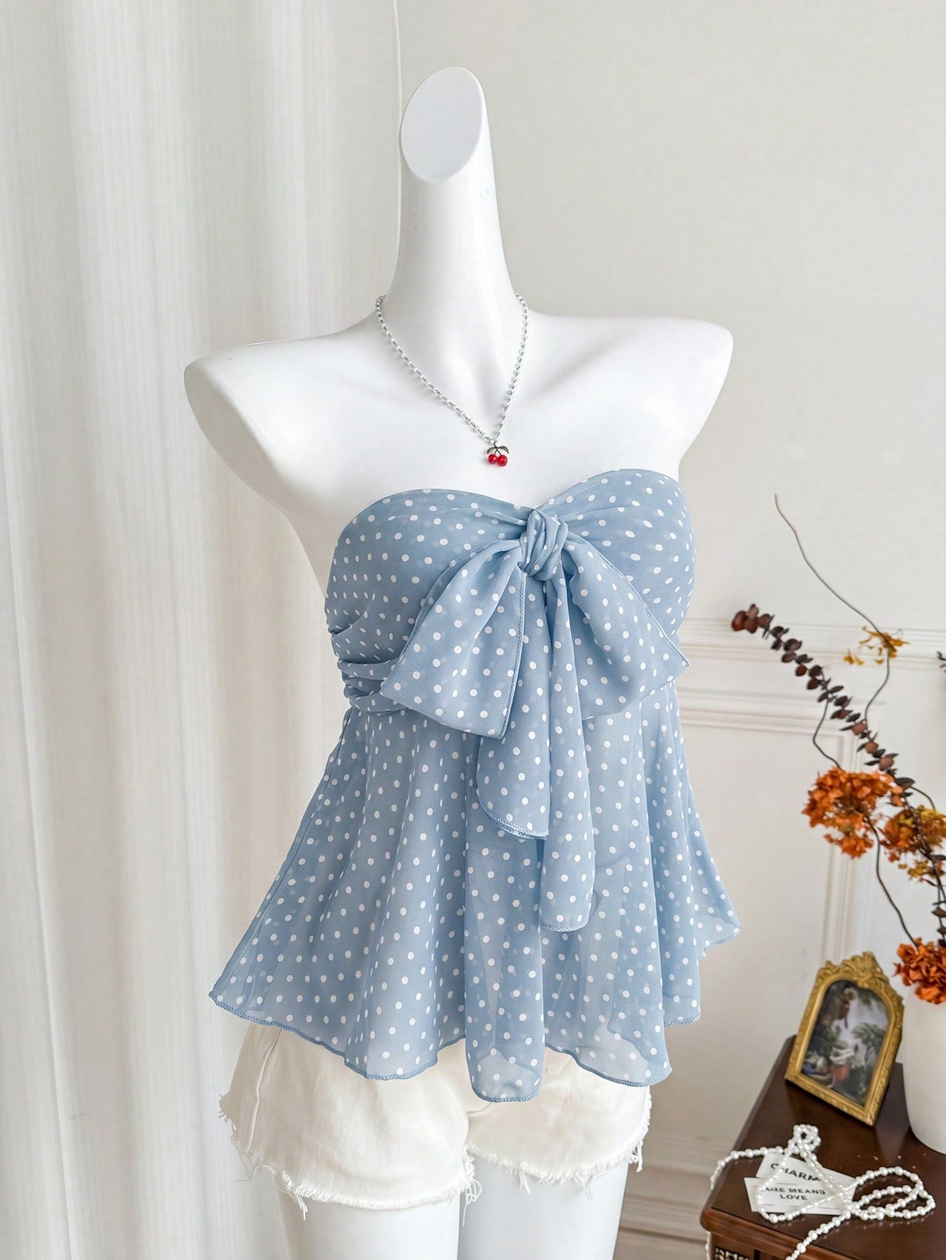 Women's polka dot strapless bandeau crop top with tie bow detail, asymmetrical shirring, and a flared hem.