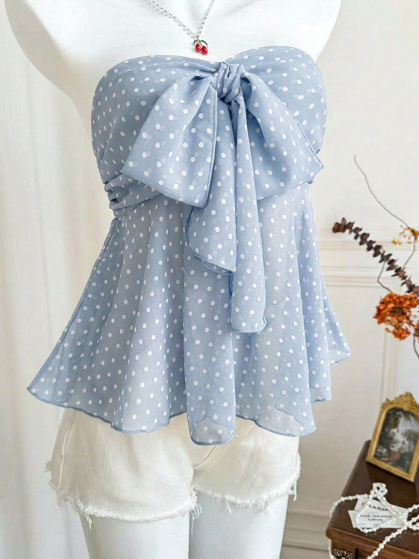 Women's polka dot strapless bandeau crop top with tie bow detail, asymmetrical shirring, and a flared hem.