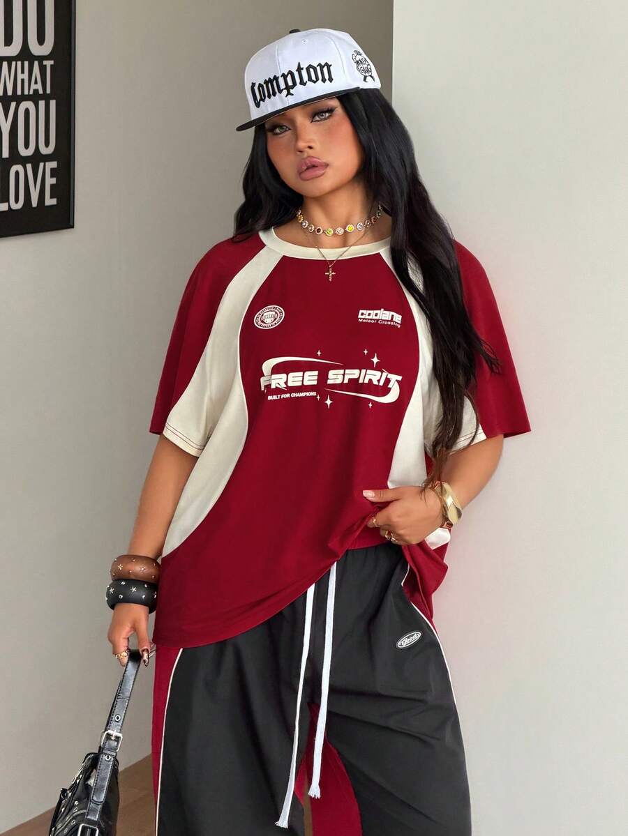 Unisex plus size oversized jersey t-shirt in brown featuring a round neck, short raglan sleeves with contrast binding, and a front letter graphic print.