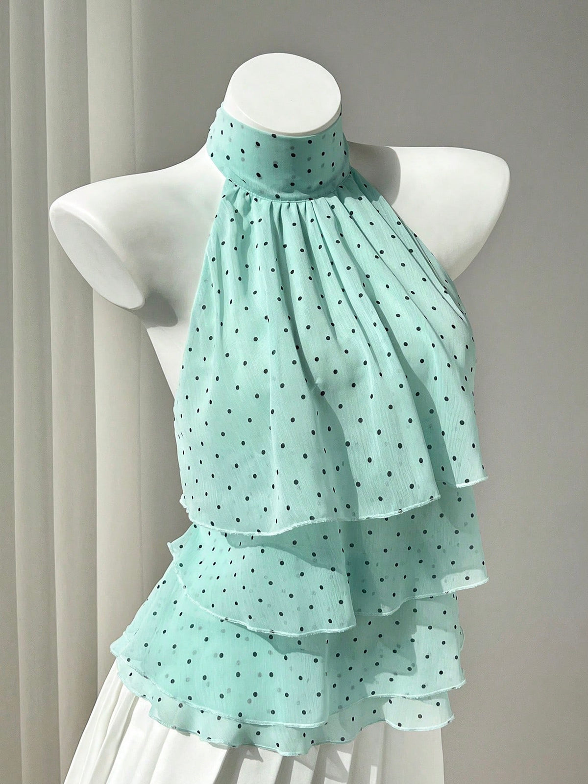 Women's white sleeveless halter neck top featuring pleated fabric, backless tie strap design, and a flared layered ruffle hem.