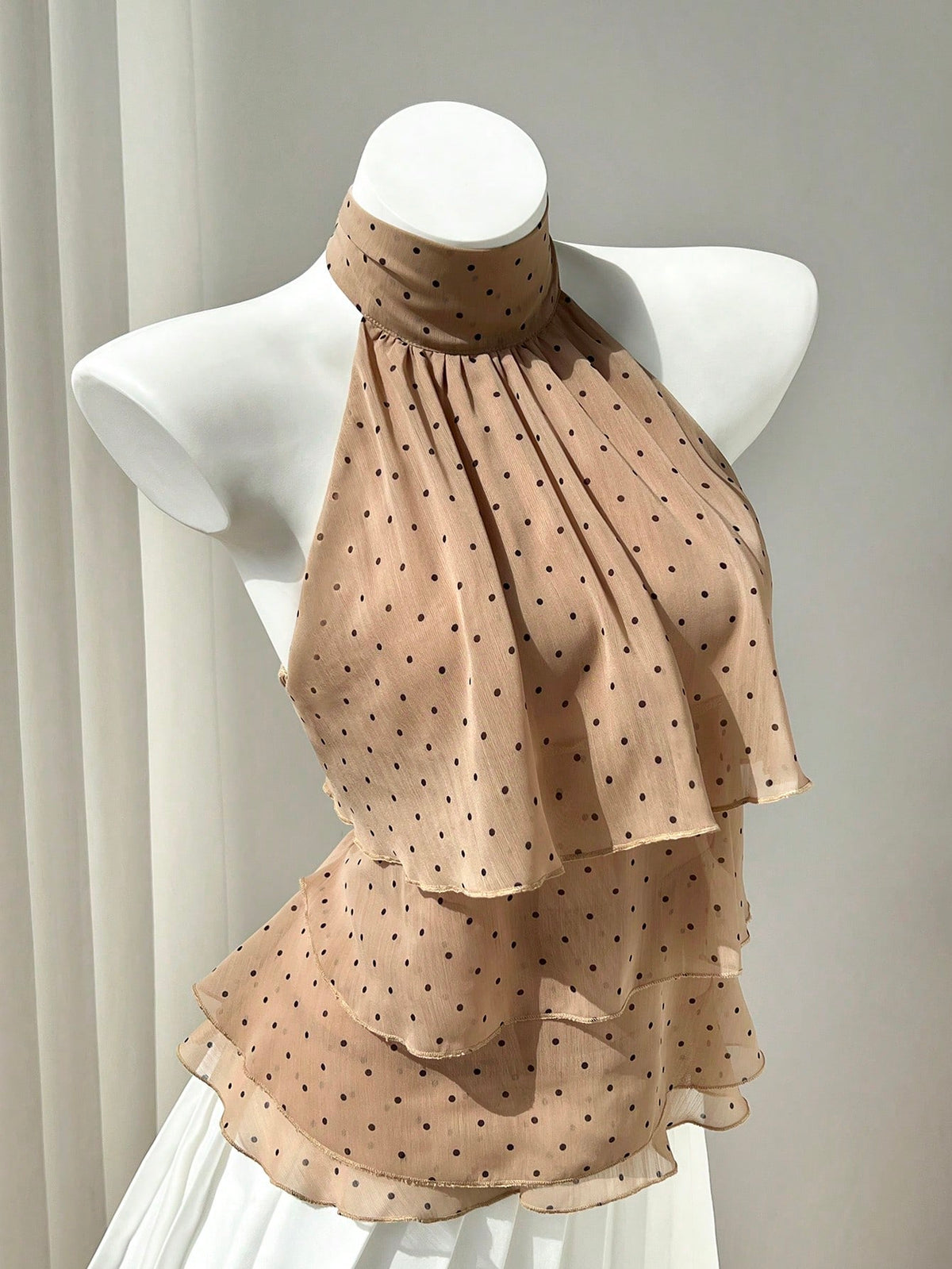 Women's white sleeveless halter neck top featuring pleated fabric, backless tie strap design, and a flared layered ruffle hem.