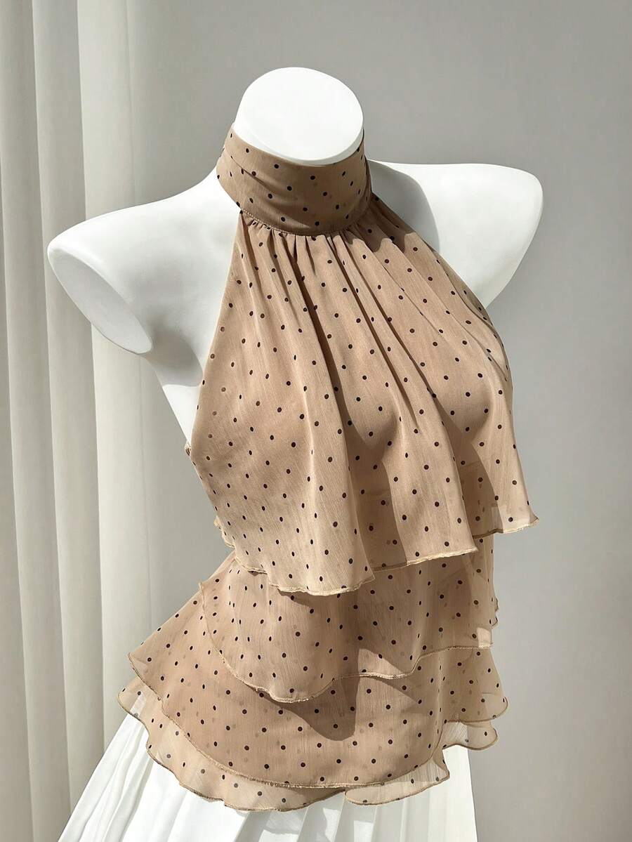 Women's white sleeveless halter neck top featuring pleated fabric, backless tie strap design, and a flared layered ruffle hem.