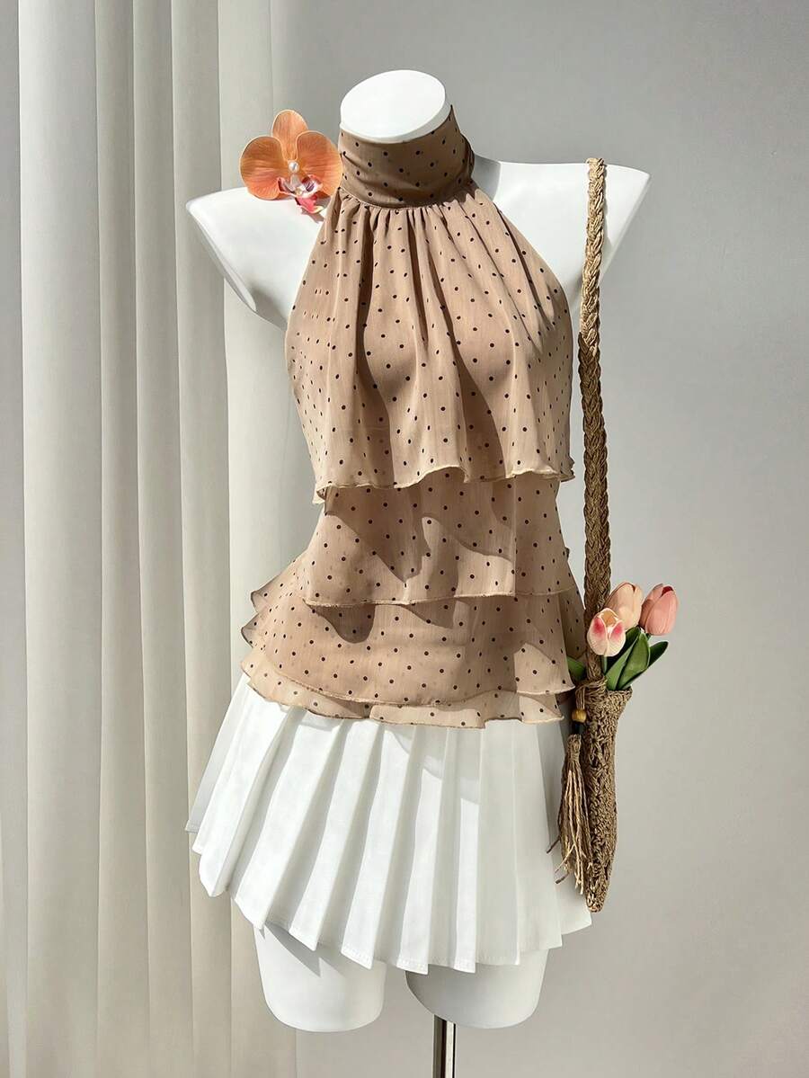 Women's white sleeveless halter neck top featuring pleated fabric, backless tie strap design, and a flared layered ruffle hem.