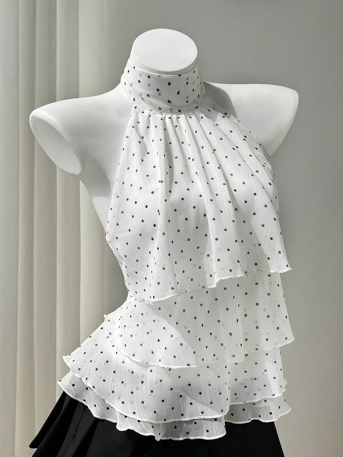 Women's white sleeveless halter neck top featuring pleated fabric, backless tie strap design, and a flared layered ruffle hem.