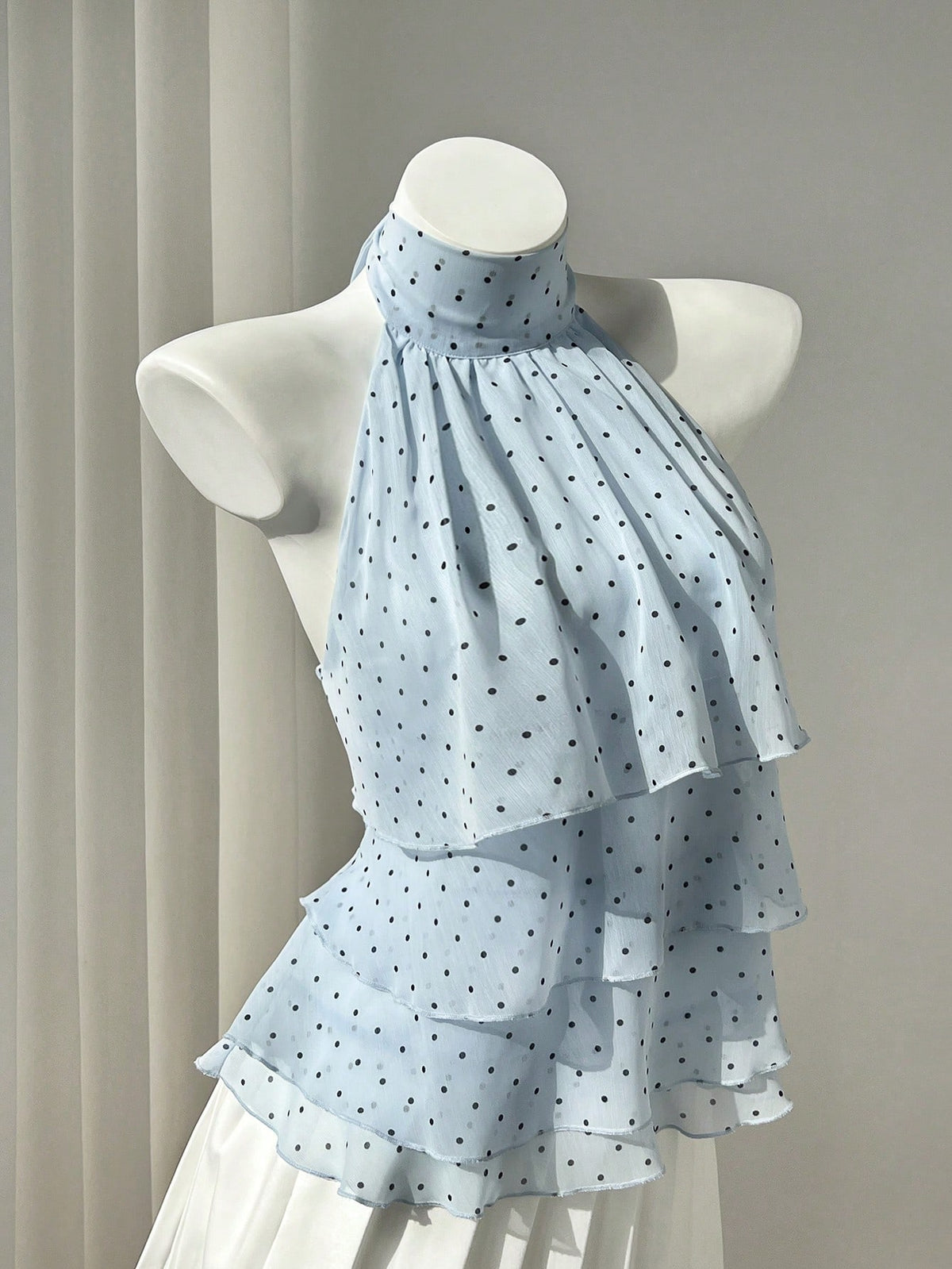 Women's white sleeveless halter neck top featuring pleated fabric, backless tie strap design, and a flared layered ruffle hem.