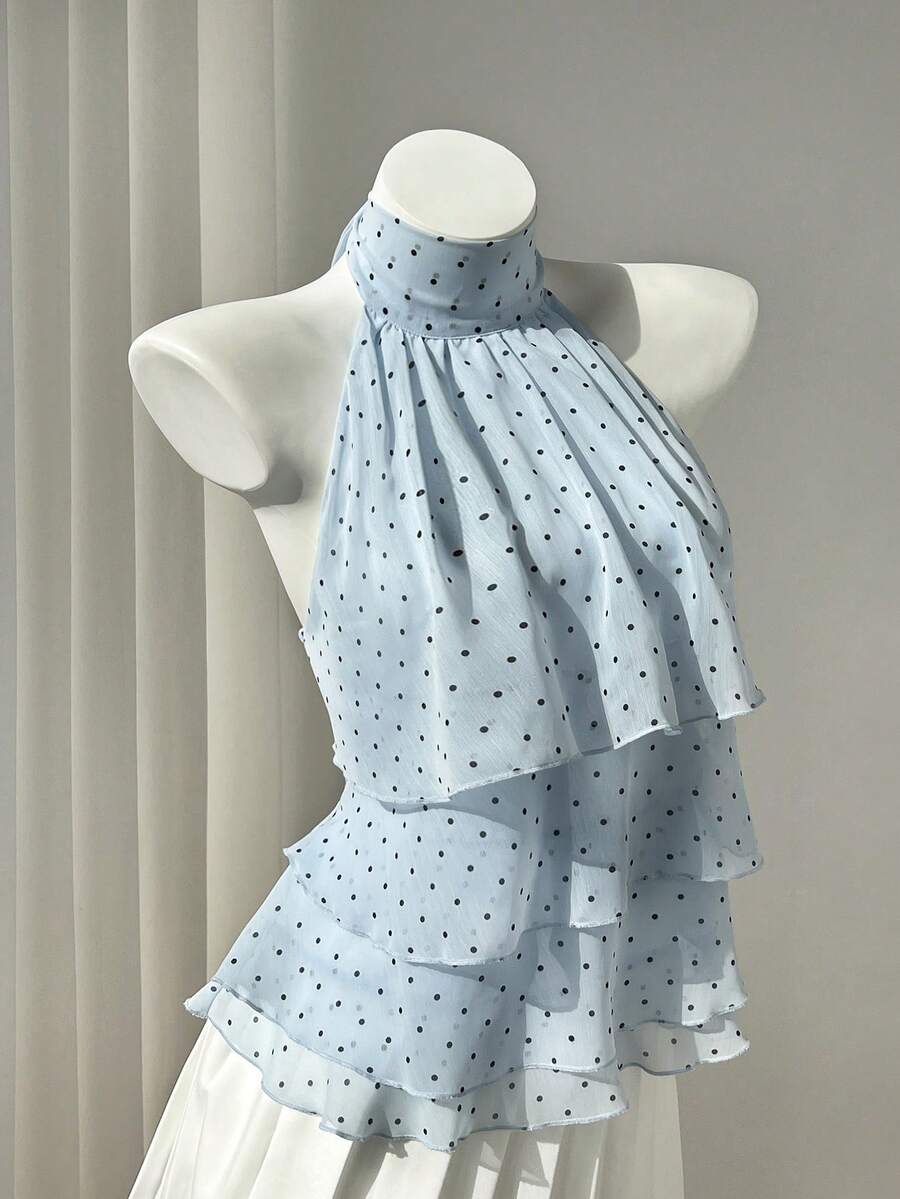 Women's white sleeveless halter neck top featuring pleated fabric, backless tie strap design, and a flared layered ruffle hem.