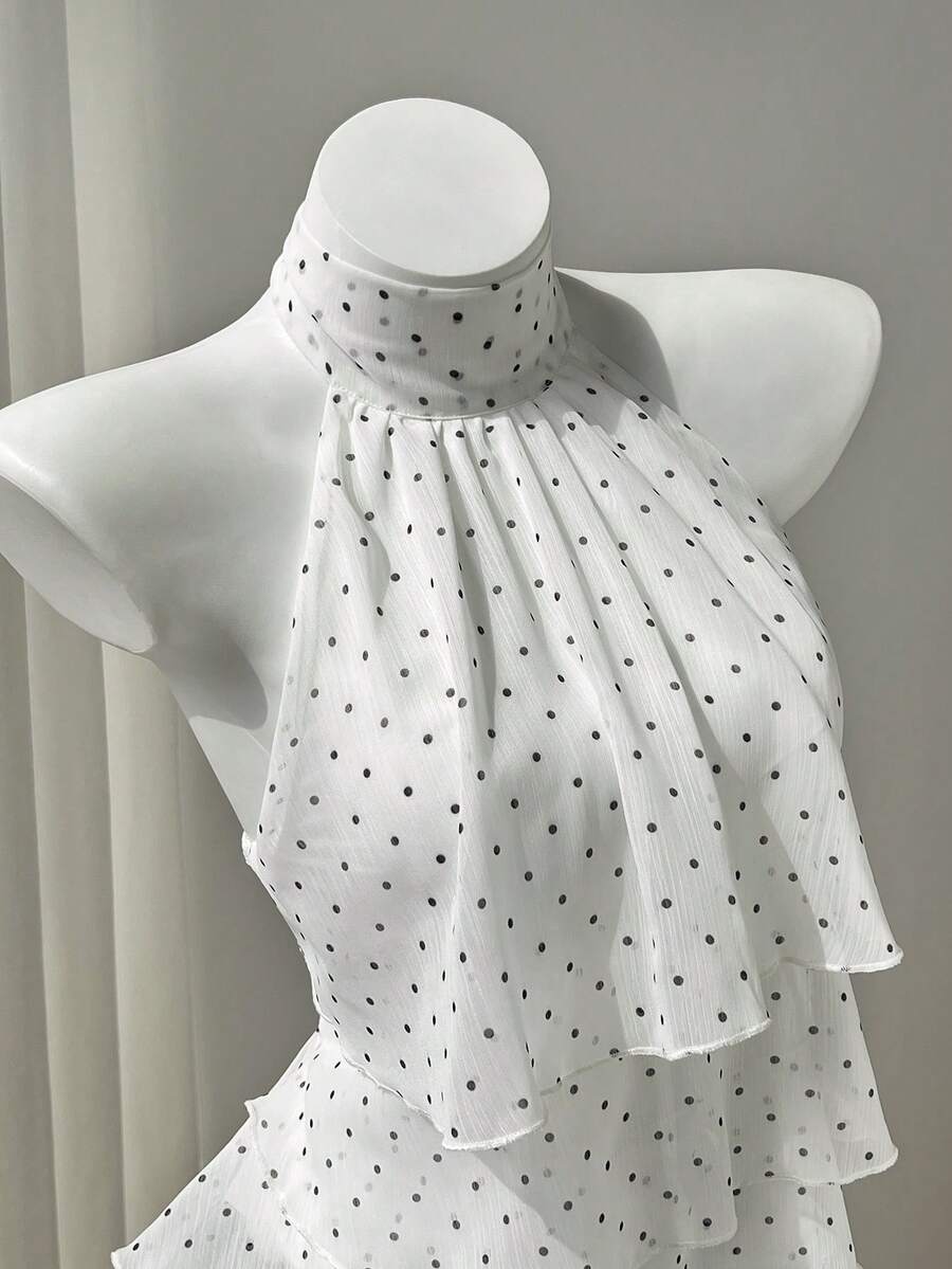 Women's white sleeveless halter neck top featuring pleated fabric, backless tie strap design, and a flared layered ruffle hem.