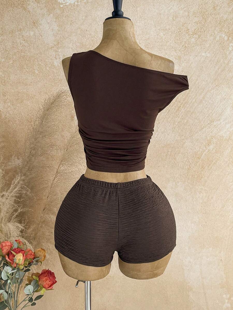 Women's black fuzzy knit two-piece set with an asymmetrical crop camisole top featuring ruched detail and cutout back, paired with matching mini shorts.