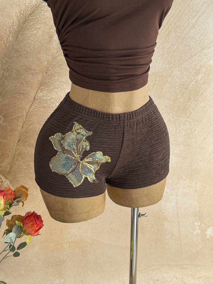 Women's black fuzzy knit two-piece set with an asymmetrical crop camisole top featuring ruched detail and cutout back, paired with matching mini shorts.