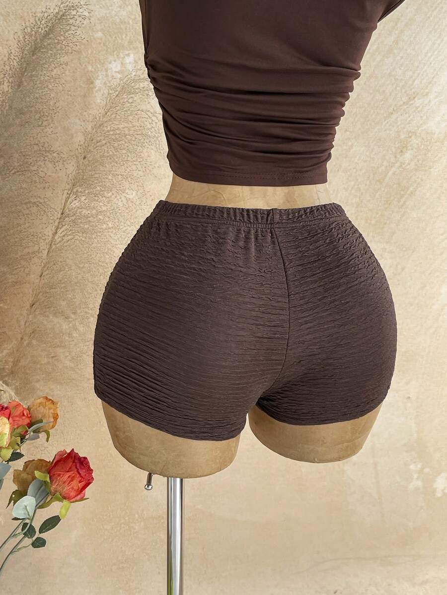 Women's black fuzzy knit two-piece set with an asymmetrical crop camisole top featuring ruched detail and cutout back, paired with matching mini shorts.