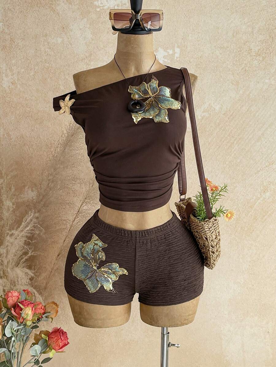 Women's black fuzzy knit two-piece set with an asymmetrical crop camisole top featuring ruched detail and cutout back, paired with matching mini shorts.