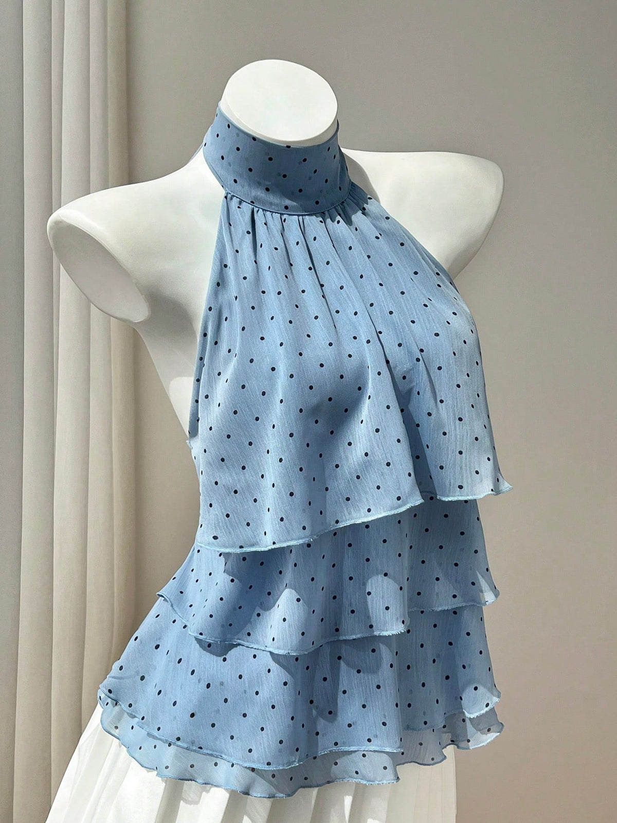Women's white sleeveless halter neck top featuring pleated fabric, backless tie strap design, and a flared layered ruffle hem.