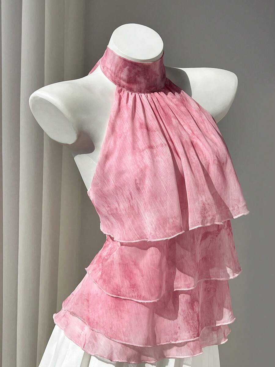Women's white sleeveless halter neck top featuring pleated fabric, backless tie strap design, and a flared layered ruffle hem.