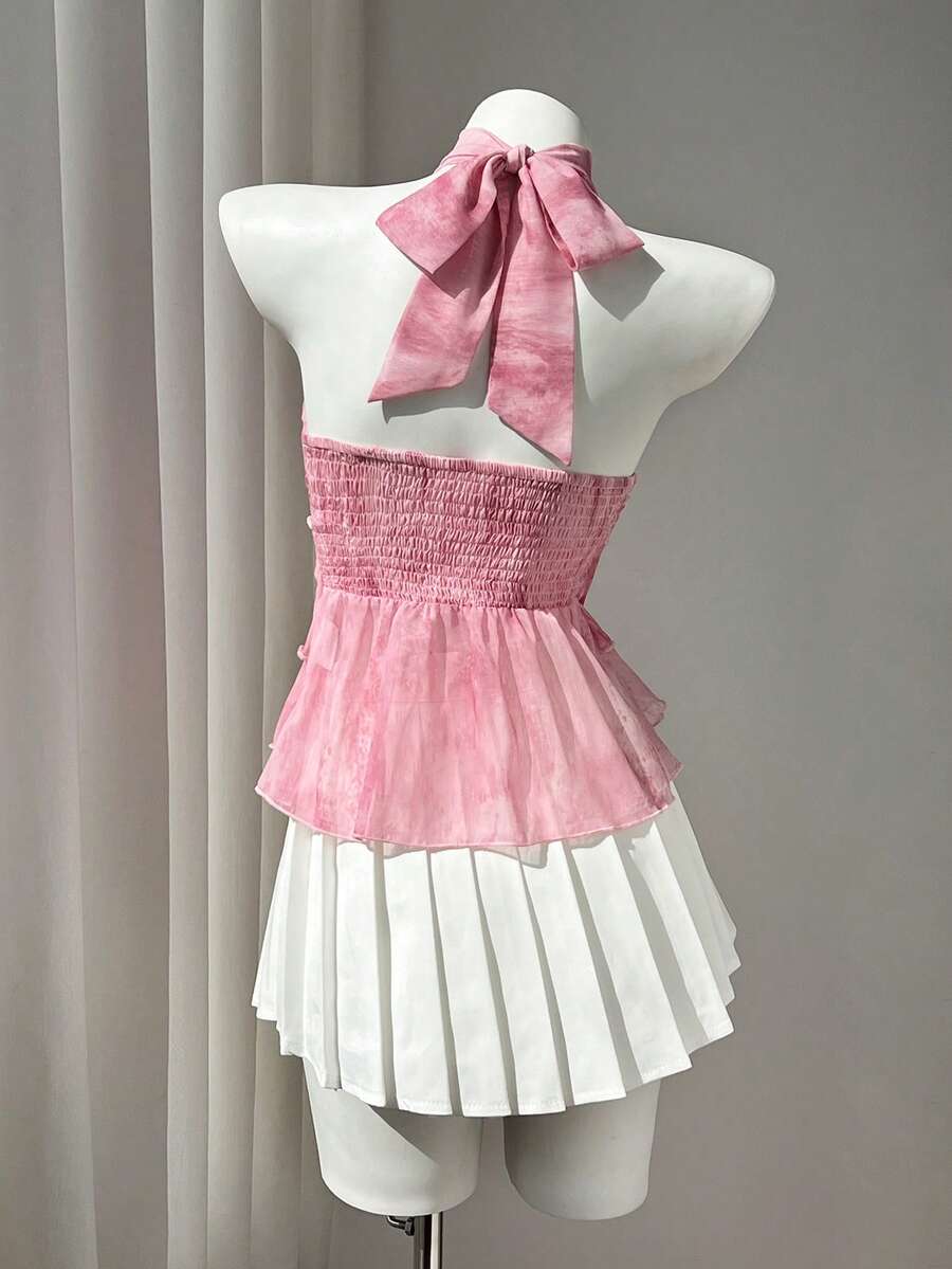 Women's white sleeveless halter neck top featuring pleated fabric, backless tie strap design, and a flared layered ruffle hem.