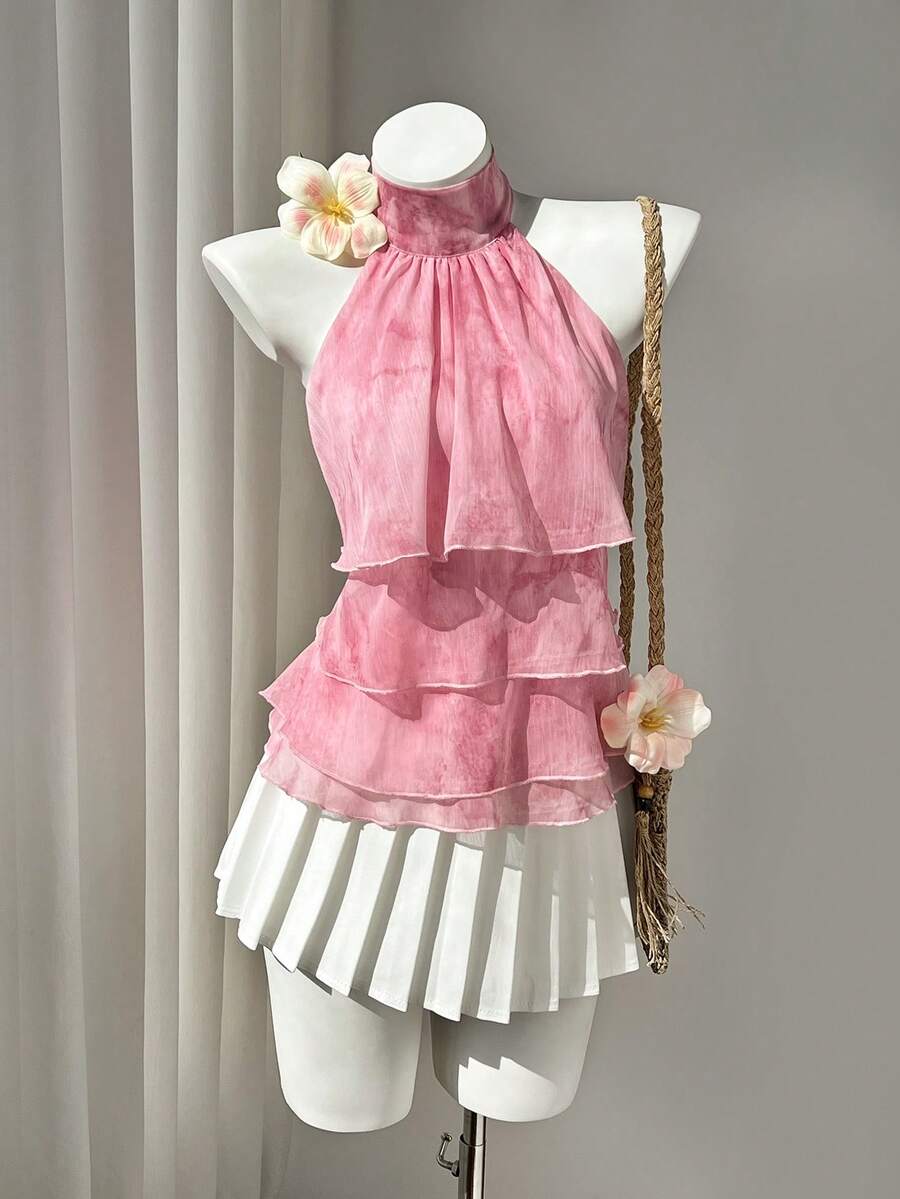 Women's white sleeveless halter neck top featuring pleated fabric, backless tie strap design, and a flared layered ruffle hem.