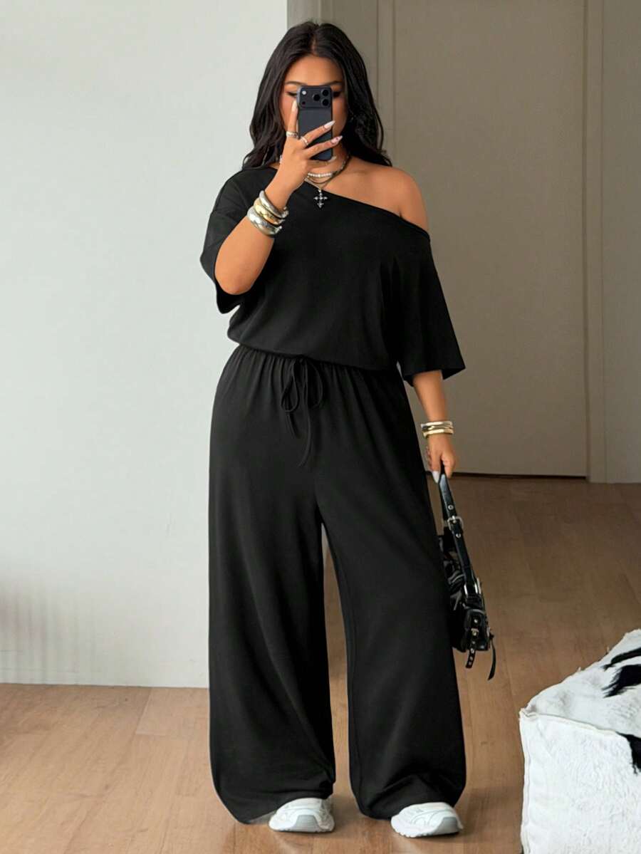Plus size women's wide leg jumpsuit in dark grey featuring an asymmetrical neckline, short batwing sleeves, and a drawstring high waist with side pockets.
