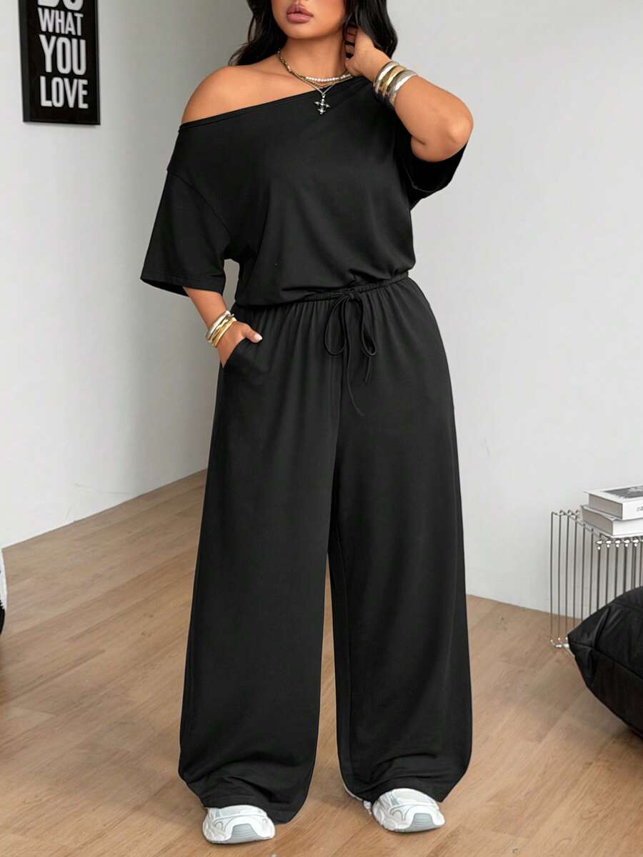 Plus size women's wide leg jumpsuit in dark grey featuring an asymmetrical neckline, short batwing sleeves, and a drawstring high waist with side pockets.