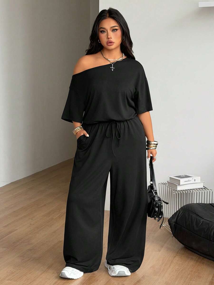 Plus size women's wide leg jumpsuit in dark grey featuring an asymmetrical neckline, short batwing sleeves, and a drawstring high waist with side pockets.
