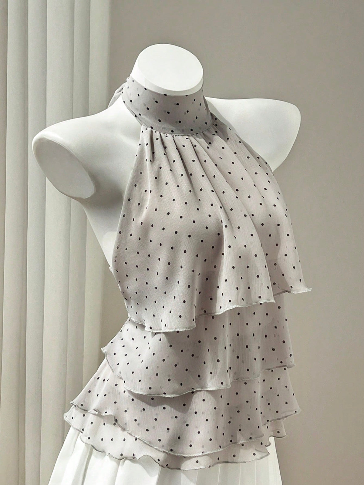 Women's white sleeveless halter neck top featuring pleated fabric, backless tie strap design, and a flared layered ruffle hem.