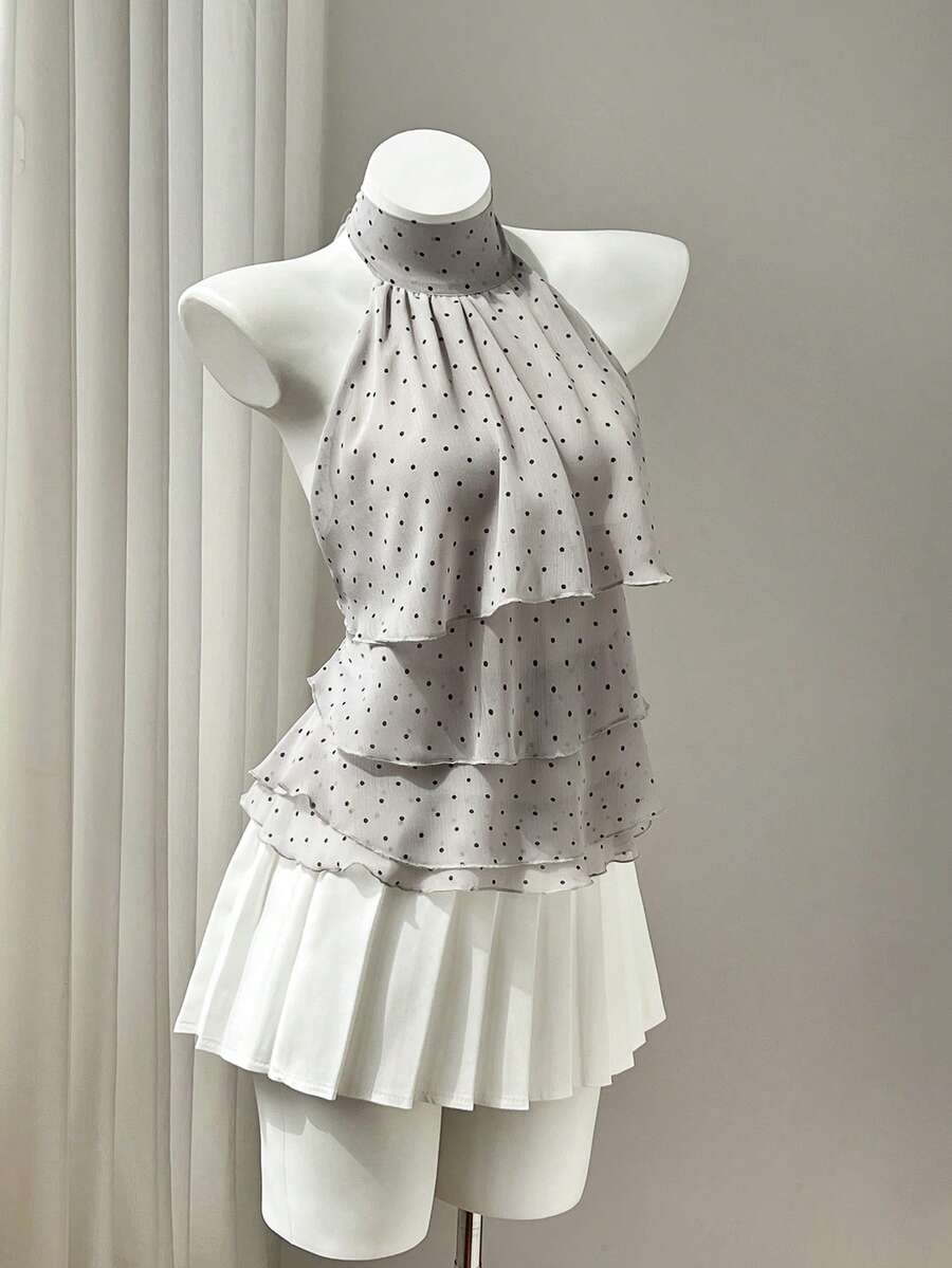 Women's white sleeveless halter neck top featuring pleated fabric, backless tie strap design, and a flared layered ruffle hem.
