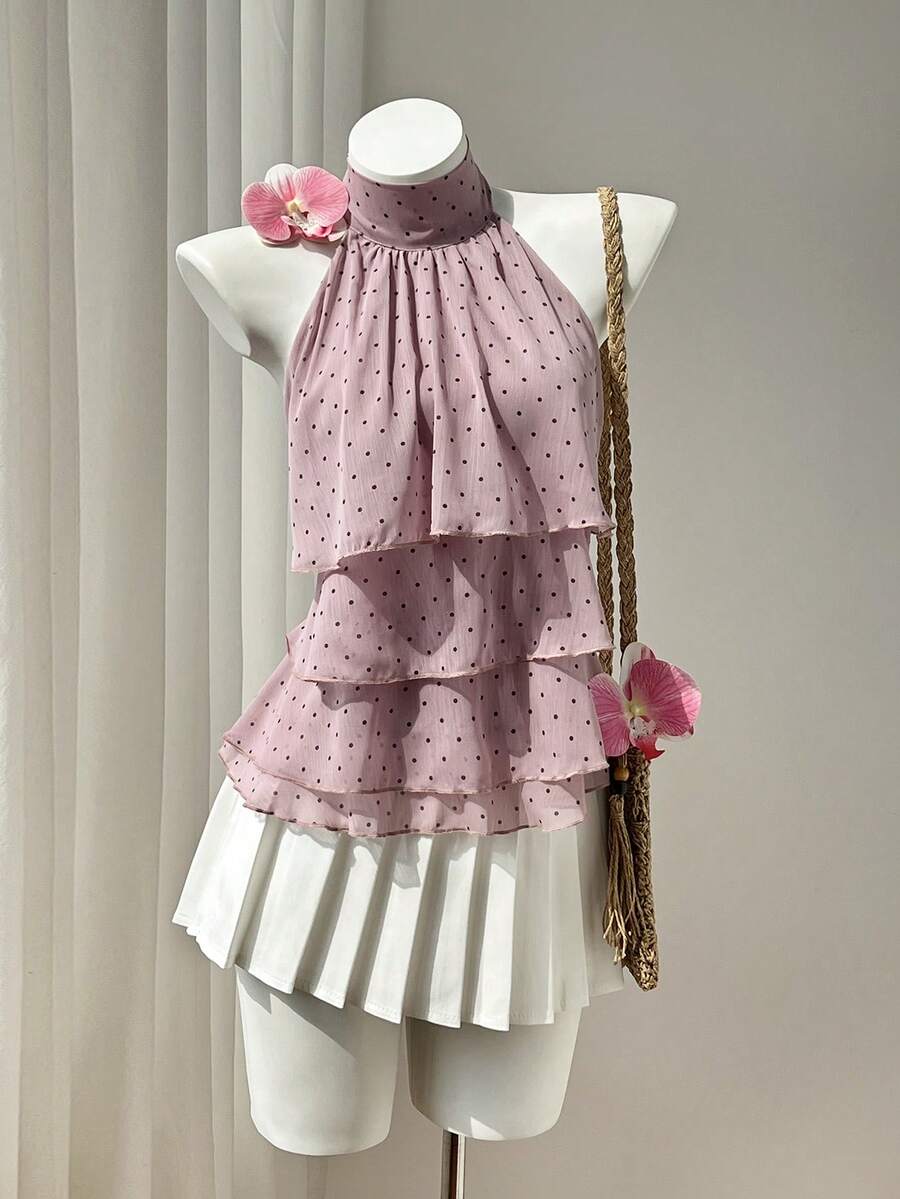 Women's white sleeveless halter neck top featuring pleated fabric, backless tie strap design, and a flared layered ruffle hem.