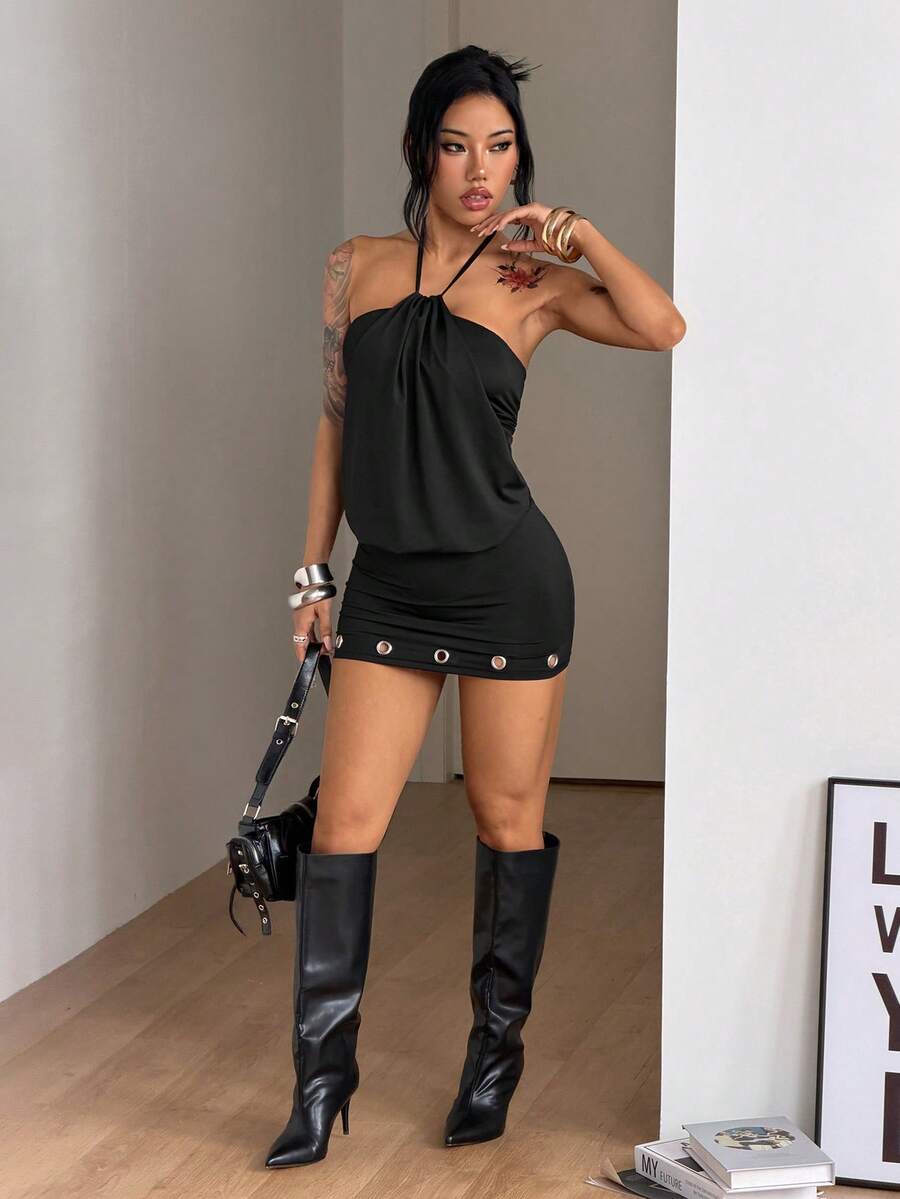 Front view of women's black halter neck mini dress featuring grommet eyelet details, a sleeveless cut, and slim fit silhouette in stretchy knitted fabric.