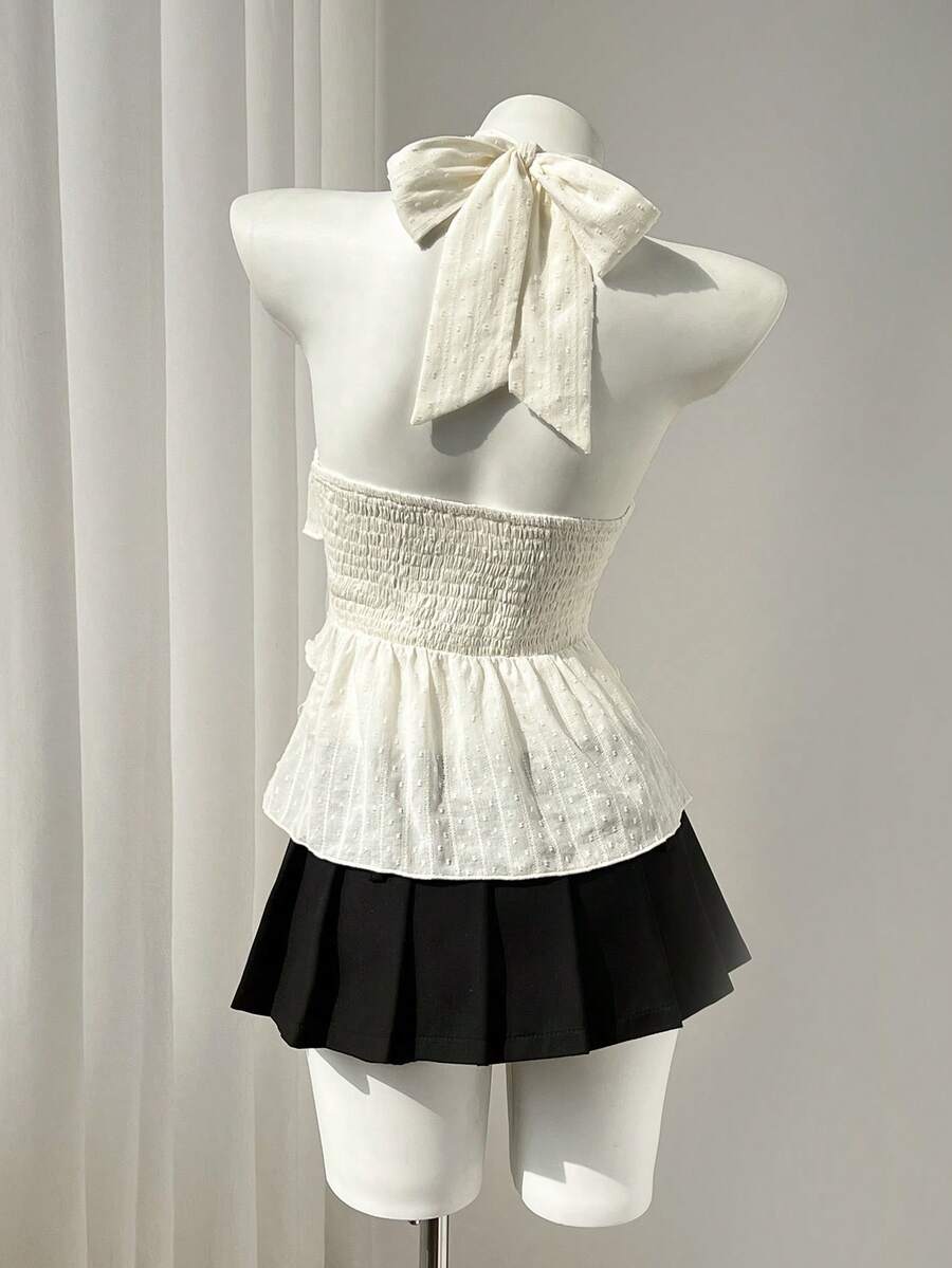 Women's white sleeveless halter neck top featuring pleated fabric, backless tie strap design, and a flared layered ruffle hem.