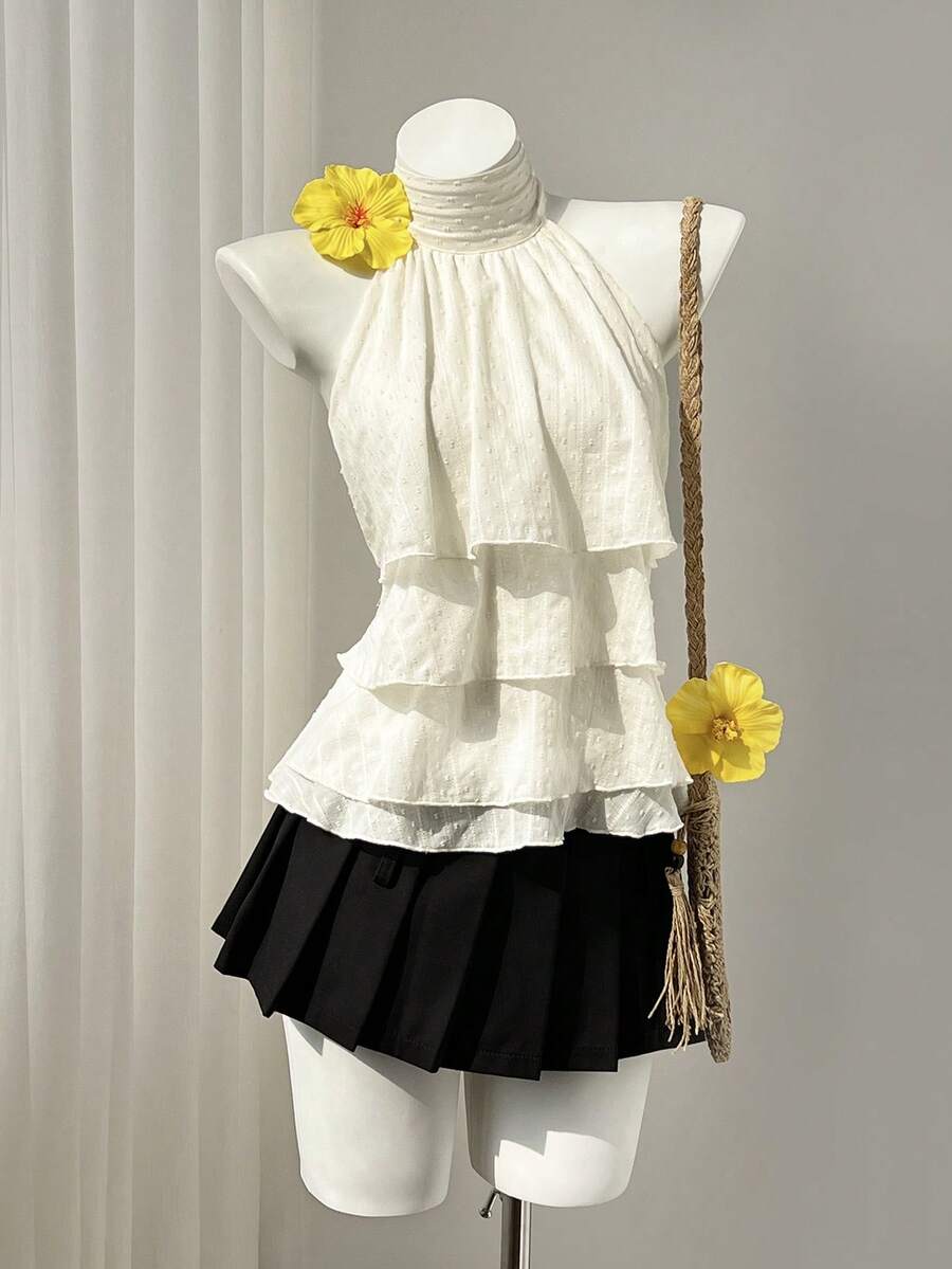 Women's white sleeveless halter neck top featuring pleated fabric, backless tie strap design, and a flared layered ruffle hem.