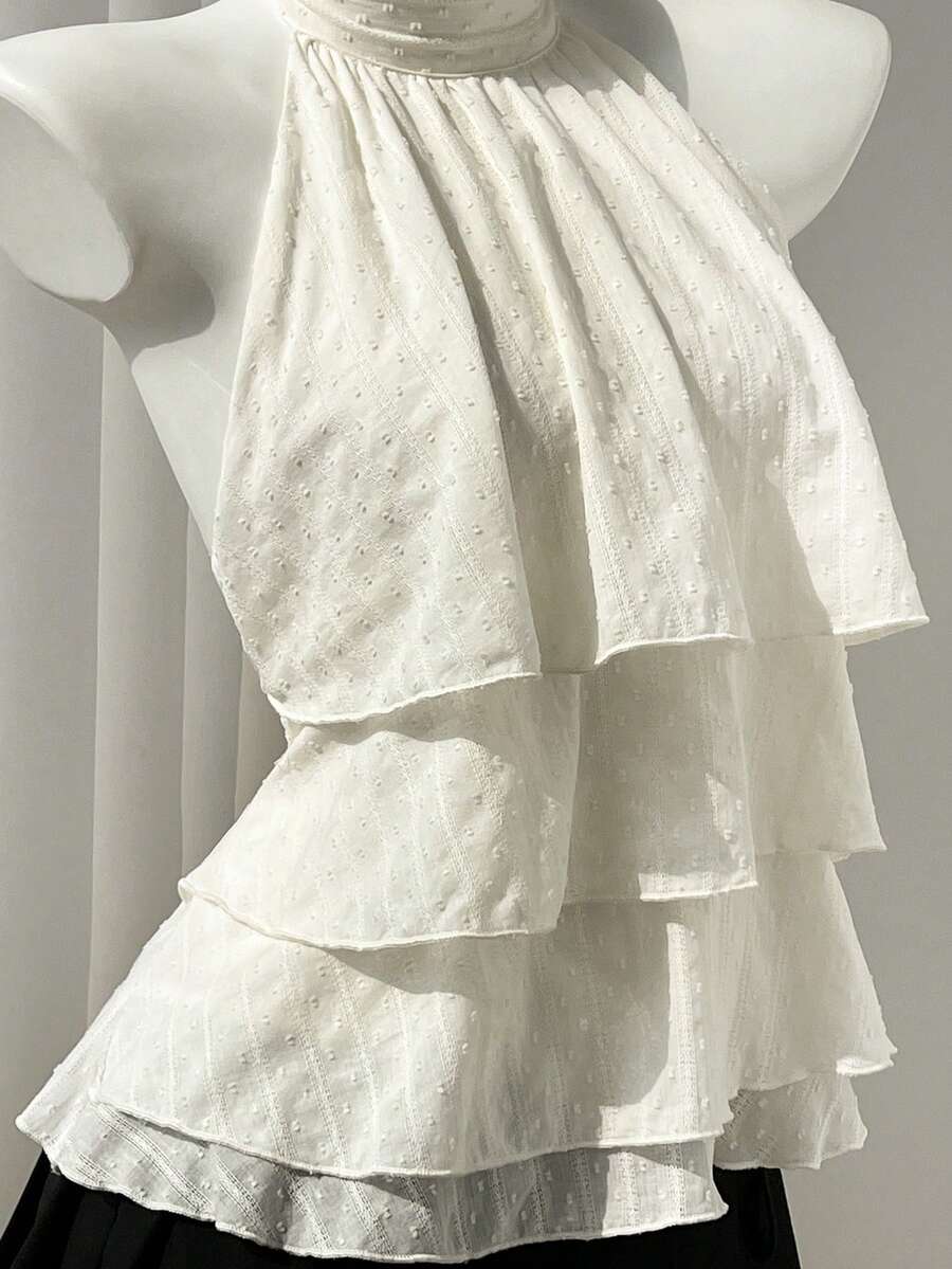 Women's white sleeveless halter neck top featuring pleated fabric, backless tie strap design, and a flared layered ruffle hem.
