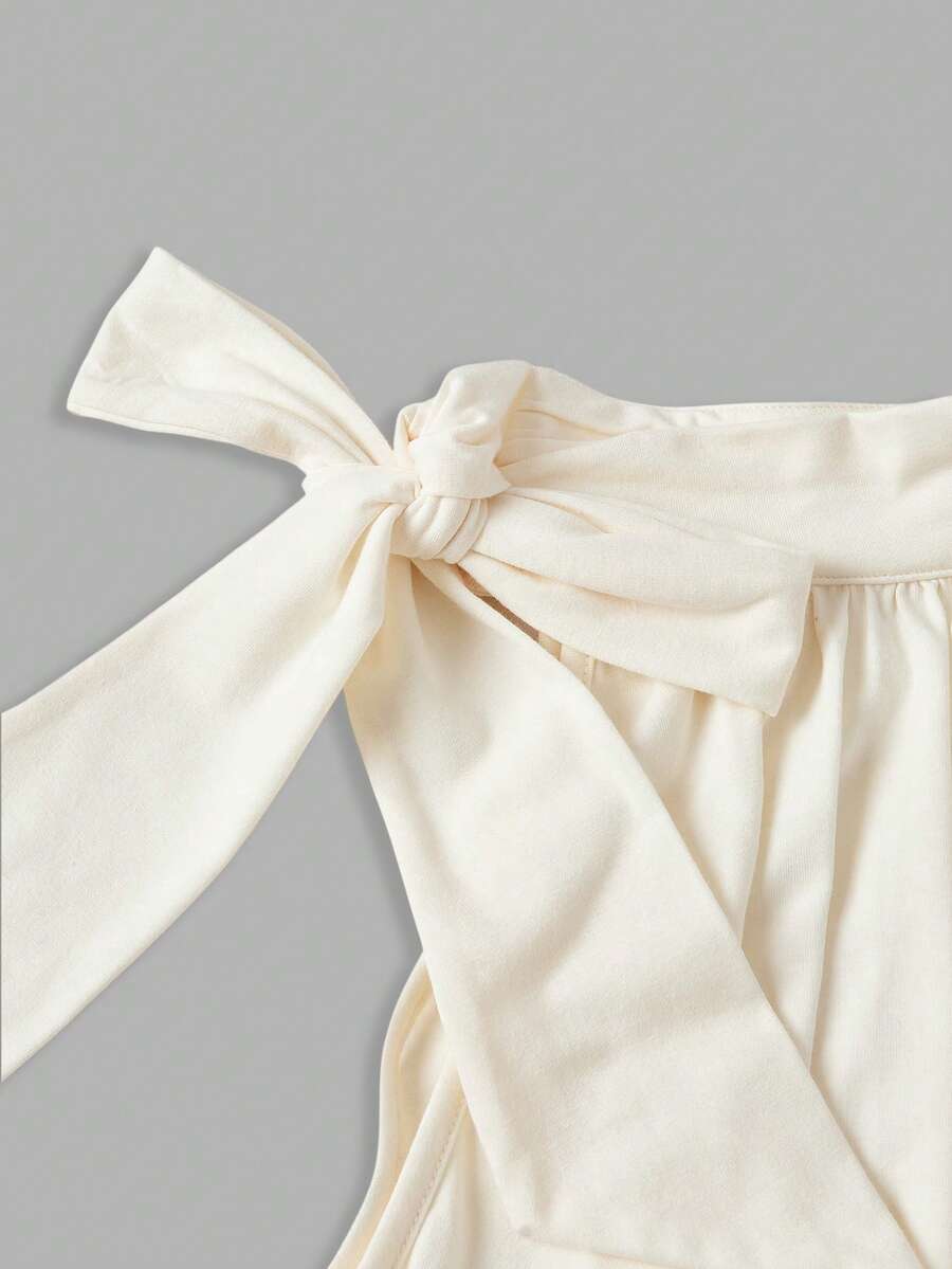 Women's sleeveless high-neck halter crop top in apricot with ruched knot front detailing.