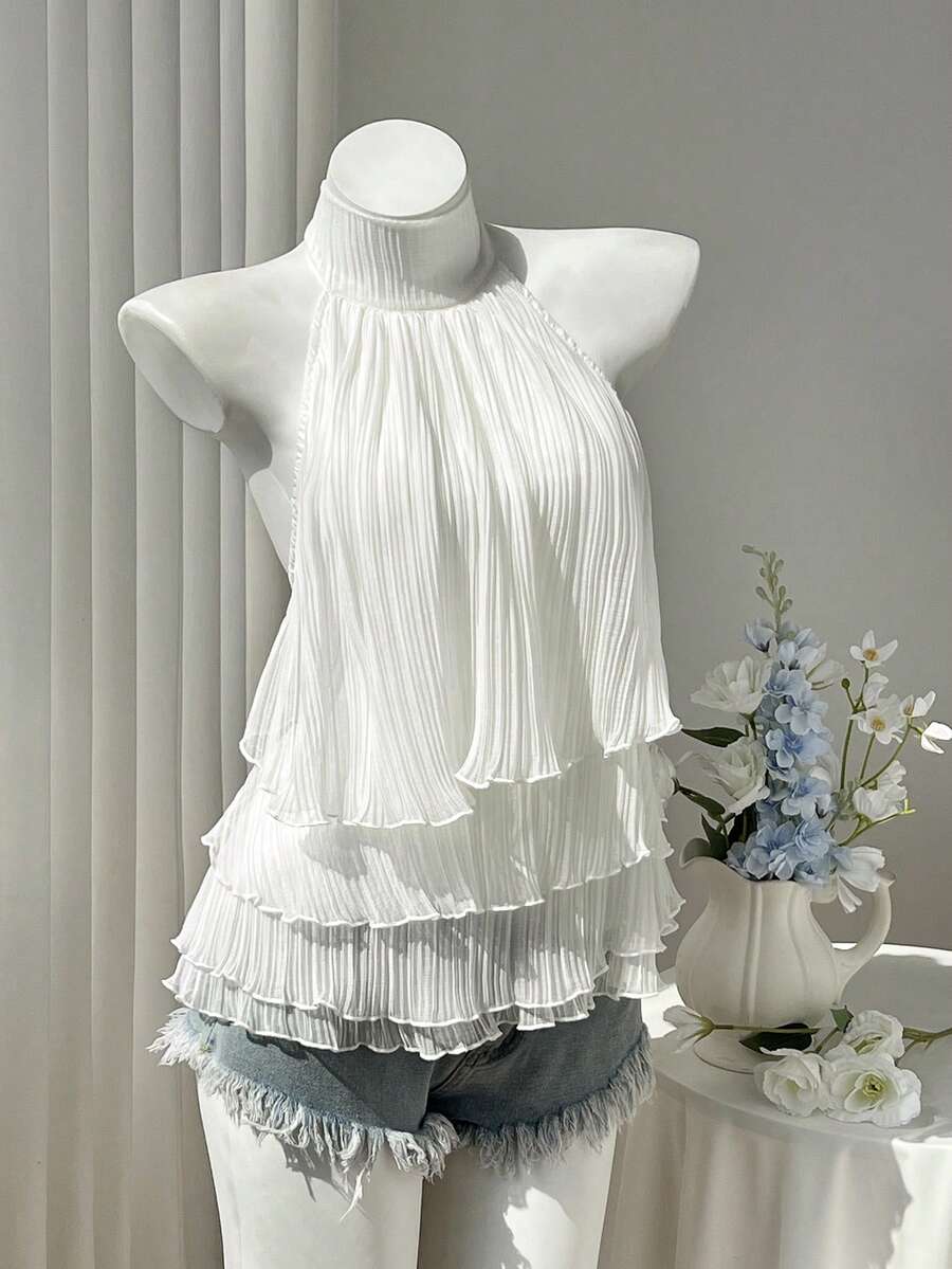 Women's white sleeveless halter neck top featuring pleated fabric, backless tie strap design, and a flared layered ruffle hem.