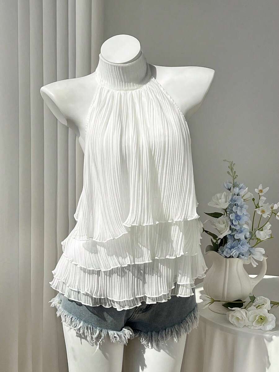 Women's white sleeveless halter neck top featuring pleated fabric, backless tie strap design, and a flared layered ruffle hem.