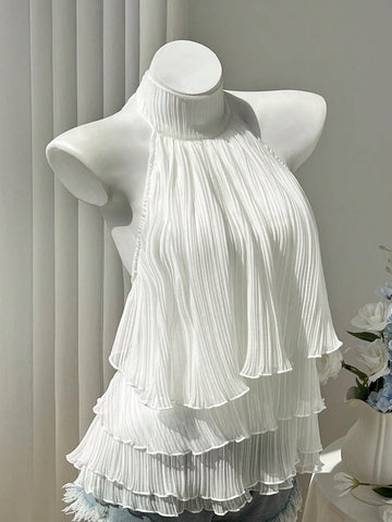 Women's white sleeveless halter neck top featuring pleated fabric, backless tie strap design, and a flared layered ruffle hem.