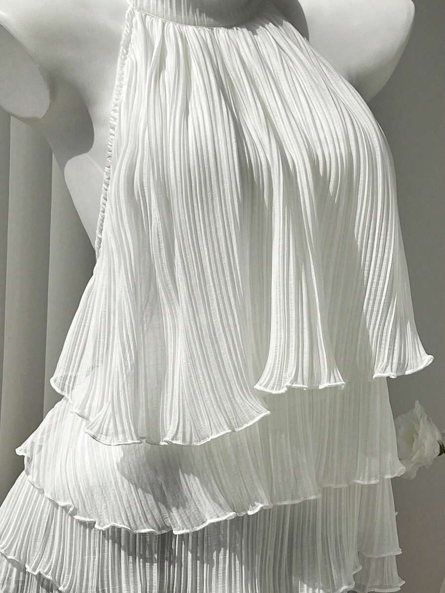 Women's white sleeveless halter neck top featuring pleated fabric, backless tie strap design, and a flared layered ruffle hem.